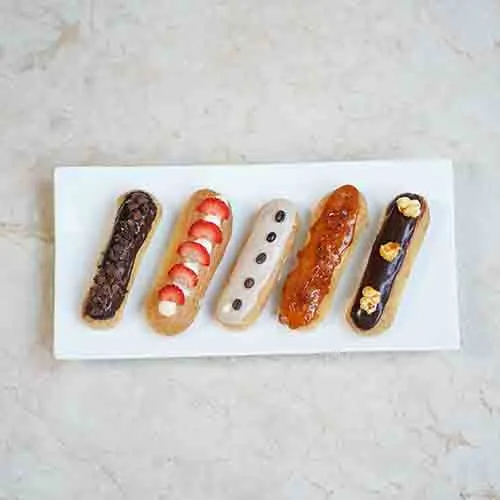 Five eclairs with different toppings lined up on a white plate